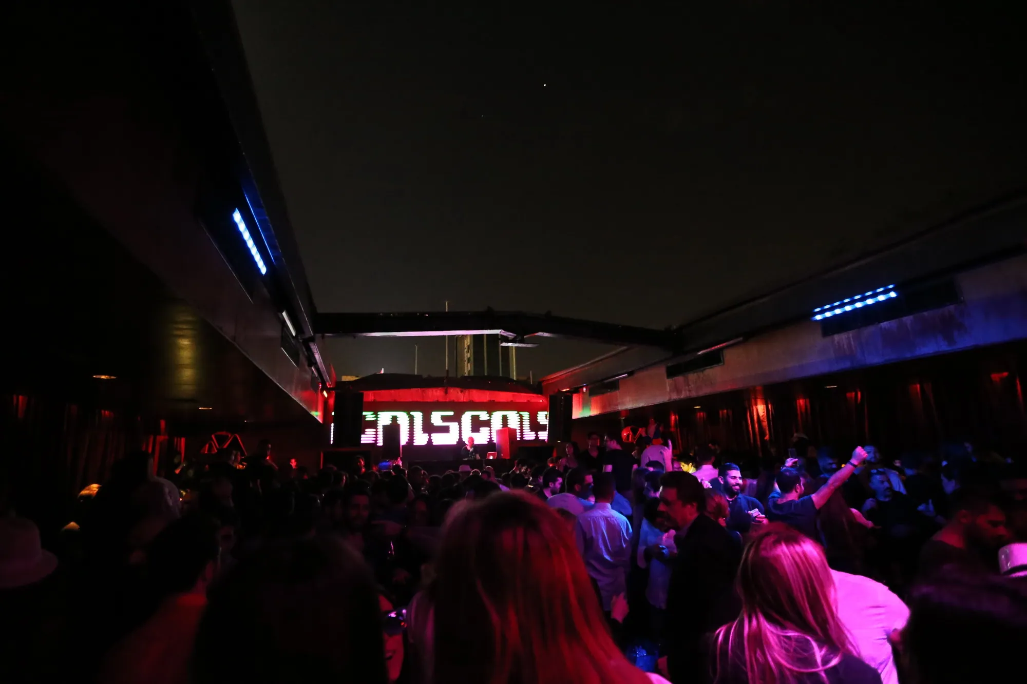 Late night club interior lit in red with the crowd close to the booth